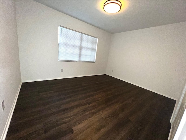 empty room with dark wood-type flooring and baseboards