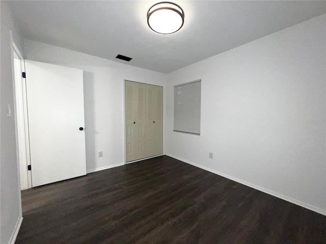 unfurnished bedroom featuring dark wood-style floors, a closet, and baseboards