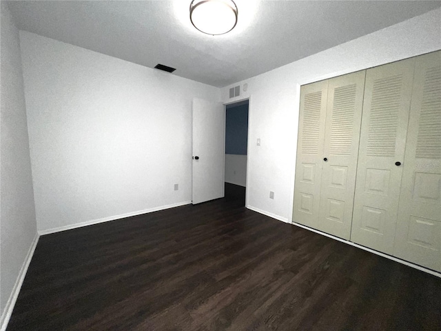 unfurnished bedroom with baseboards, visible vents, dark wood finished floors, and a closet