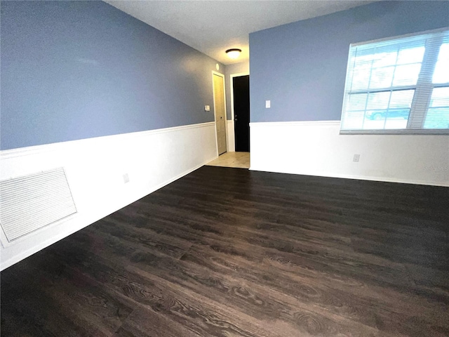 unfurnished room with a wainscoted wall, visible vents, and wood finished floors