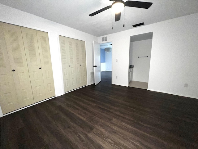 unfurnished bedroom featuring wood finished floors, visible vents, and two closets