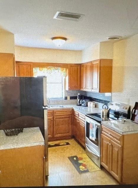 kitchen featuring visible vents, light countertops, stainless steel range with electric stovetop, and brown cabinets