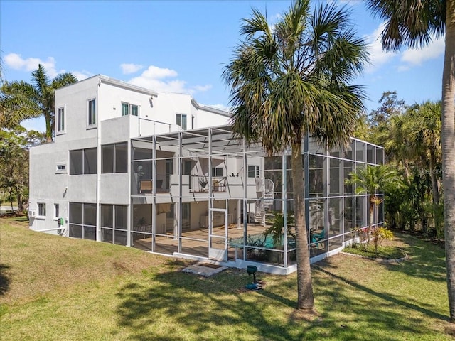 rear view of property with stucco siding, a patio, glass enclosure, and a yard