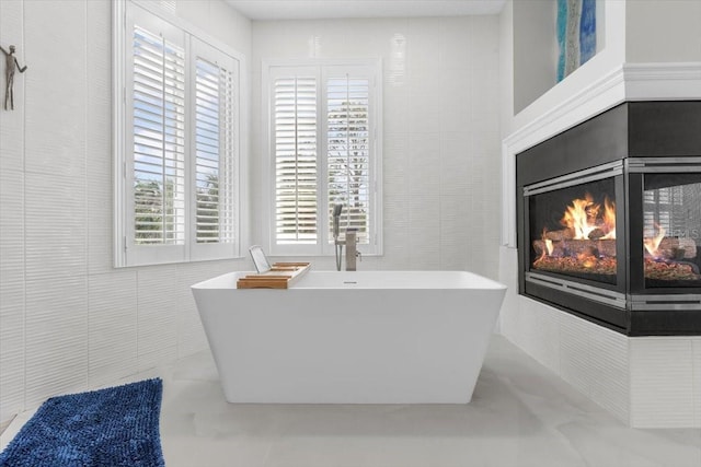 bathroom with a multi sided fireplace, tile walls, and a freestanding tub