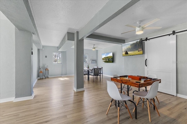 dining area featuring baseboards, ceiling fan, a textured ceiling, a barn door, and light wood-type flooring