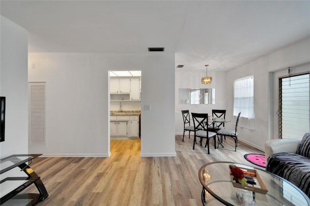 living area with a notable chandelier, light wood finished floors, visible vents, and baseboards