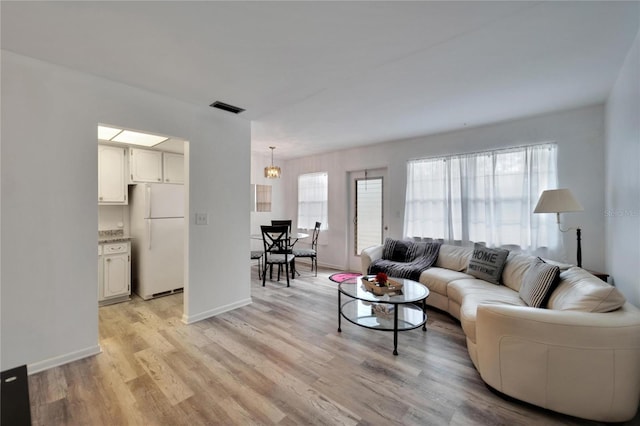 living area featuring baseboards, visible vents, and light wood finished floors