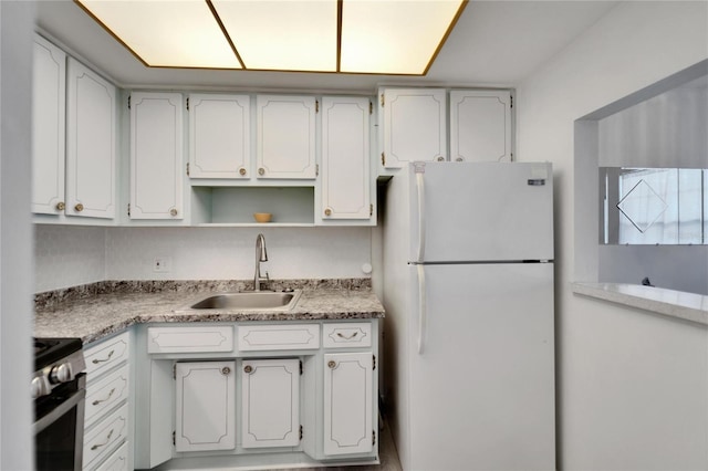 kitchen with a sink, white cabinetry, light countertops, freestanding refrigerator, and stainless steel electric range oven