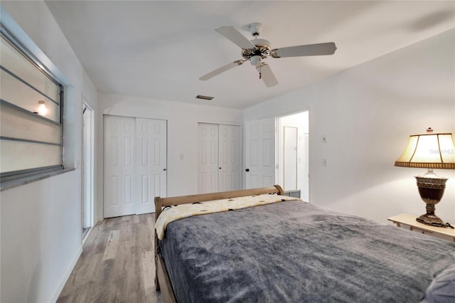 bedroom with two closets, visible vents, light wood-style floors, a ceiling fan, and baseboards