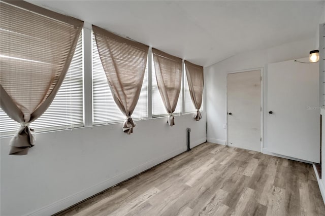 empty room with light wood-style floors, lofted ceiling, and baseboards