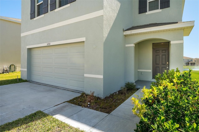 property entrance featuring a garage, driveway, and stucco siding