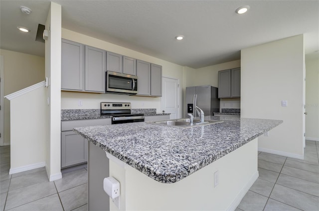 kitchen featuring stainless steel appliances, an island with sink, gray cabinetry, and light tile patterned floors