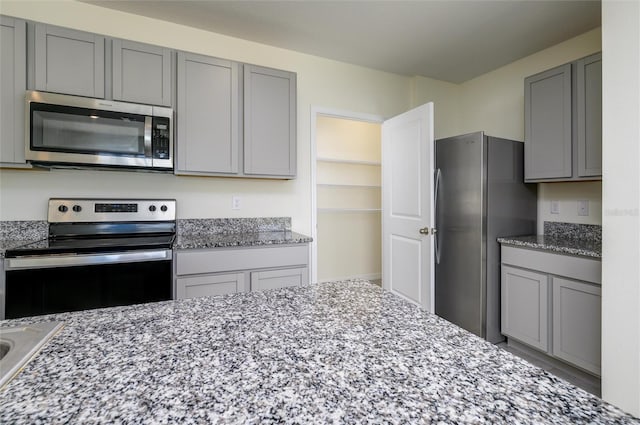 kitchen with gray cabinets, light stone counters, and stainless steel appliances