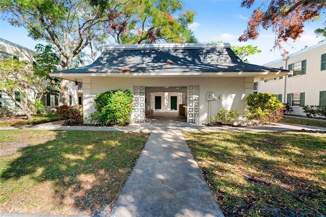 view of front of house featuring a shingled roof, a front yard, french doors, and stucco siding