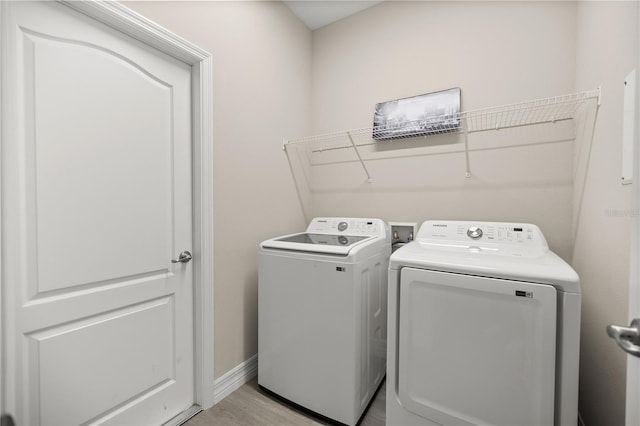 clothes washing area with baseboards, light wood-style flooring, laundry area, and washer and clothes dryer