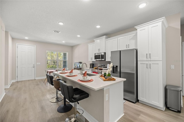 kitchen featuring a center island with sink, a kitchen bar, light wood-type flooring, appliances with stainless steel finishes, and white cabinetry