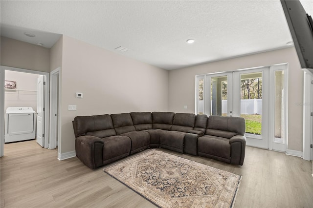 living area with washer / clothes dryer, light wood-style floors, baseboards, and a textured ceiling