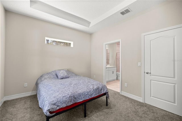 bedroom featuring visible vents, light carpet, ensuite bathroom, a tray ceiling, and baseboards