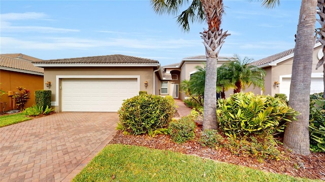 view of front of home featuring an attached garage, a tiled roof, decorative driveway, and stucco siding