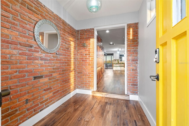 hallway featuring baseboards, brick wall, and wood finished floors