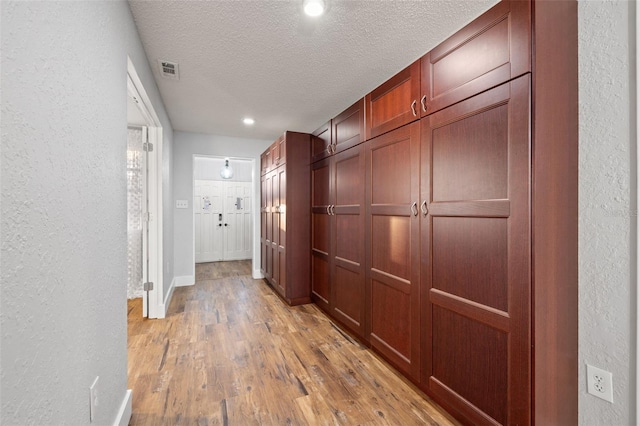 hall featuring a textured ceiling, a textured wall, and light wood finished floors