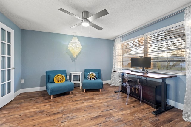 sitting room with a textured ceiling, baseboards, wood finished floors, and ceiling fan with notable chandelier