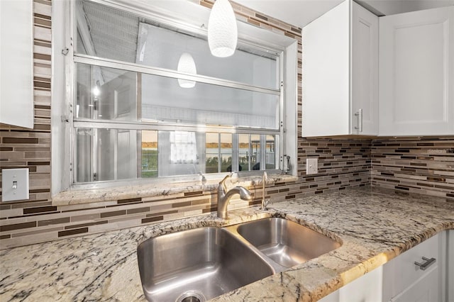 kitchen with backsplash, a sink, light stone countertops, and white cabinets