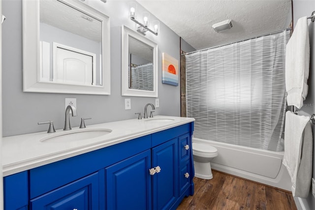 bathroom with a textured ceiling, double vanity, wood finished floors, and a sink