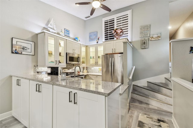 kitchen with light stone counters, stainless steel appliances, backsplash, glass insert cabinets, and a peninsula