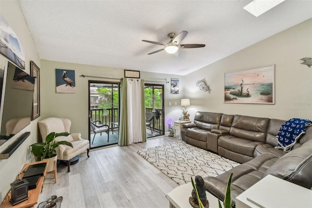 living area featuring a textured ceiling, ceiling fan, a skylight, and light wood-style flooring