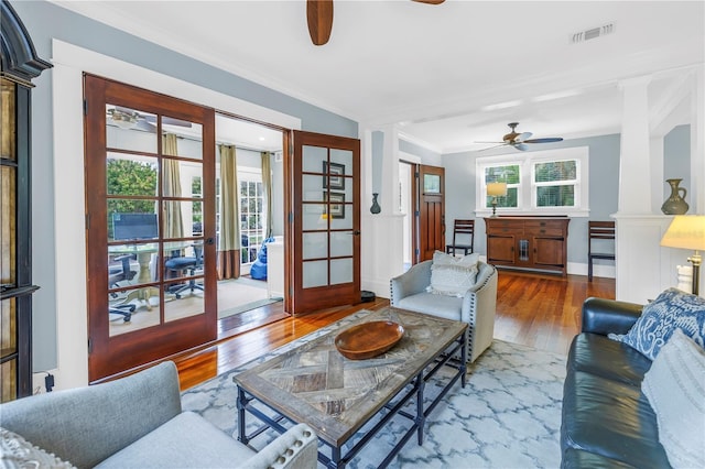 living room featuring crown molding, wood-type flooring, visible vents, a ceiling fan, and ornate columns