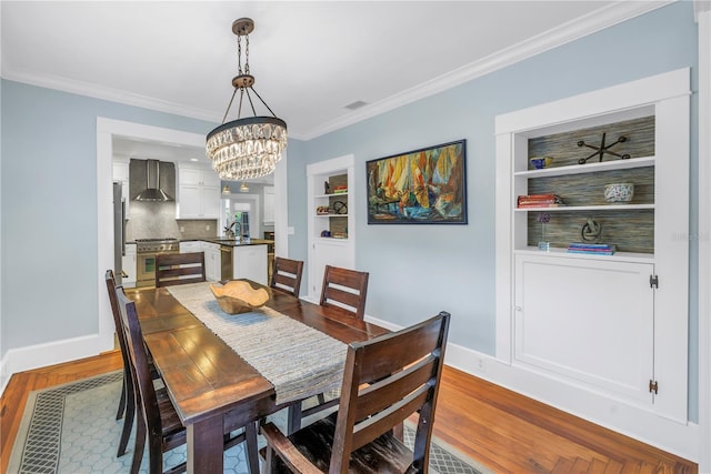 dining space with built in features, dark wood-style flooring, crown molding, and baseboards