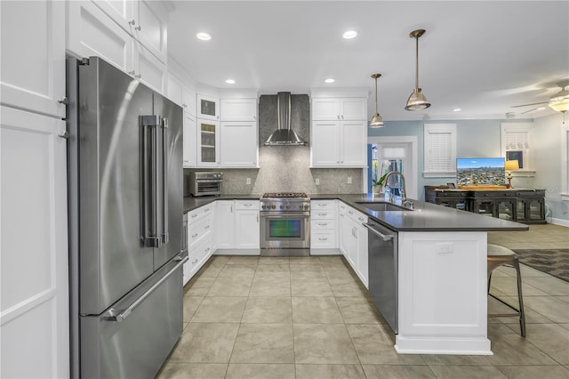 kitchen with premium appliances, dark countertops, a sink, a peninsula, and wall chimney exhaust hood