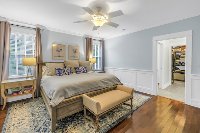 bedroom featuring a decorative wall, a ceiling fan, wainscoting, hardwood / wood-style floors, and crown molding