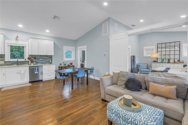 living area featuring dark wood-style floors, visible vents, a barn door, vaulted ceiling, and plenty of natural light