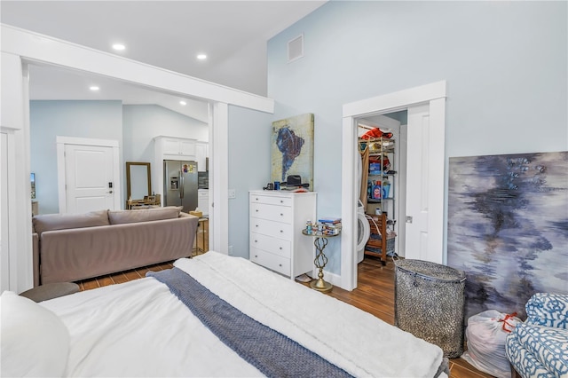 bedroom featuring wood finished floors, visible vents, vaulted ceiling, a closet, and stainless steel fridge