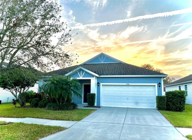 view of front of property featuring a garage, concrete driveway, a lawn, and roof with shingles