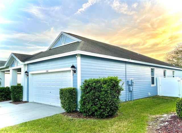 view of side of property featuring a garage, driveway, a shingled roof, a lawn, and fence