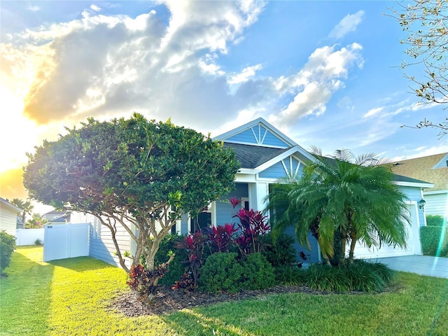 obstructed view of property featuring a garage, fence, a yard, concrete driveway, and roof with shingles