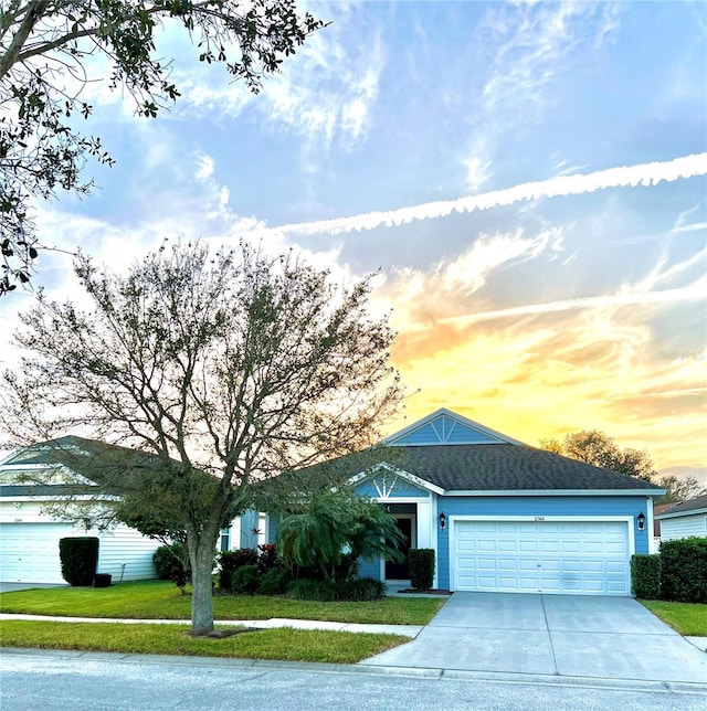 single story home with driveway, a shingled roof, a garage, and a front lawn