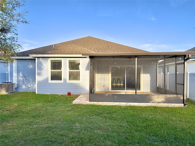 back of property with a sunroom, a shingled roof, central AC, and a lawn