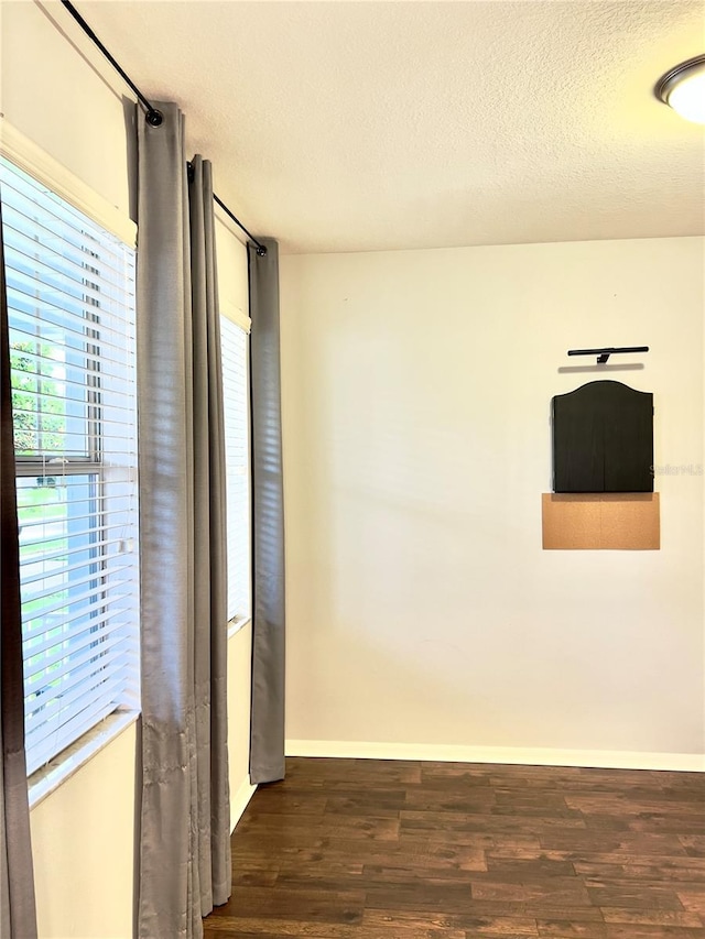 unfurnished room featuring a wealth of natural light, a textured ceiling, baseboards, and wood finished floors