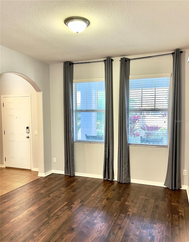 spare room with arched walkways, dark wood finished floors, a textured ceiling, and baseboards