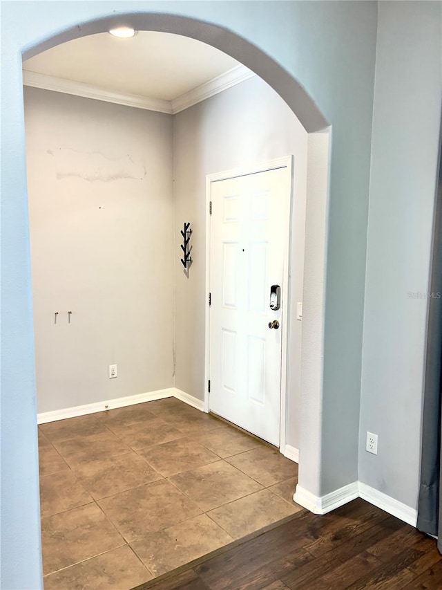 entryway featuring arched walkways, ornamental molding, wood finished floors, and baseboards