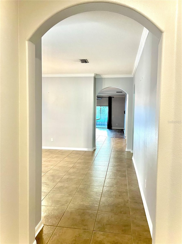 hall featuring baseboards, visible vents, arched walkways, tile patterned floors, and crown molding