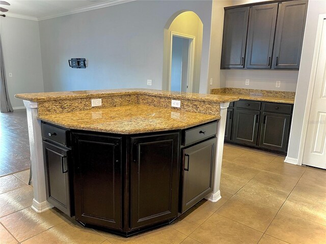 kitchen with light tile patterned floors, arched walkways, a kitchen island, light stone countertops, and crown molding