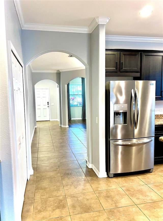 kitchen with arched walkways, crown molding, stainless steel refrigerator with ice dispenser, light tile patterned floors, and baseboards