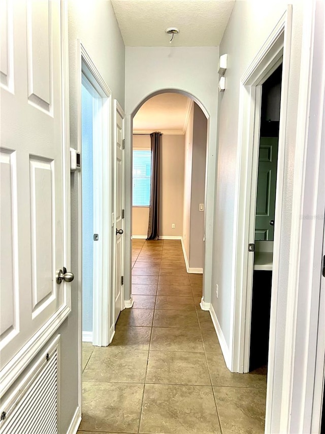 hallway with baseboards, arched walkways, and light tile patterned flooring