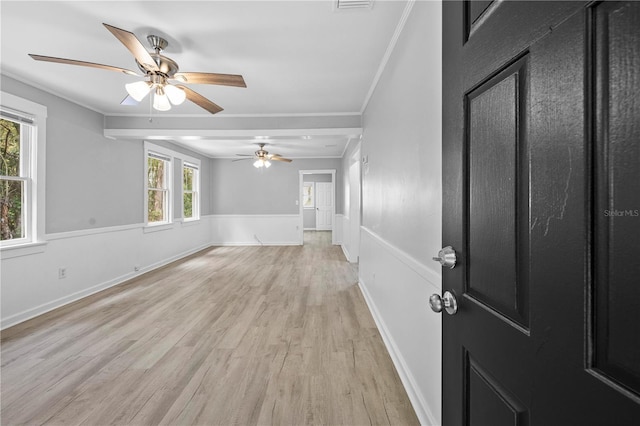 interior space with light wood finished floors, crown molding, ceiling fan, baseboards, and a wainscoted wall