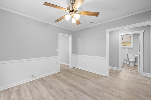 unfurnished room with visible vents, crown molding, ceiling fan, wainscoting, and wood finished floors